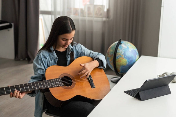 Nastolatka uczy się grać na gitarze w domu za pomocą lekcji online. Hobby zdalnej edukacji muzycznej gitara akustyczna. Odbiór. Wysokiej jakości zdjęcie - Zdjęcie, obraz