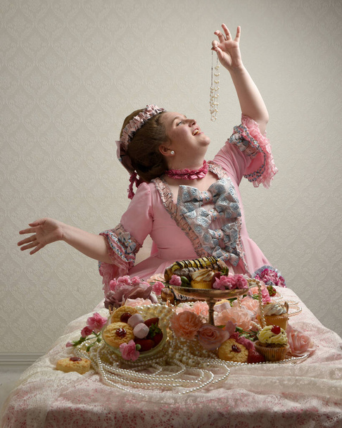 Close up portret uroczej modelki w przestronnej różowej sukni, kostium historycznej francuskiej szlachty barokowej. siedząc przy stole ze słodkimi ciastkami i pobłażliwą ucztą. - Zdjęcie, obraz