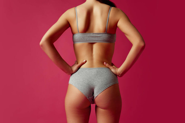 Rear view, cropped portrait of young woman holds hands on hips against magenta studio background. Anti-cellulite. Concept of beauty treatments, dieting, female health, femininity, plastic surgery. - Photo, Image