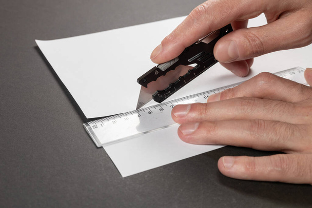 Mies leikkaa paperia paperiveitsellä ja viivoittimella lähikuva. - Valokuva, kuva