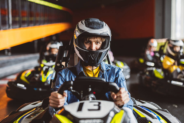 Kart-Rennen Nahaufnahme des konzentrierten Jungen im Karren mit Helm vor dem Start, der Rest der Fahrer im Hintergrund - Foto, Bild