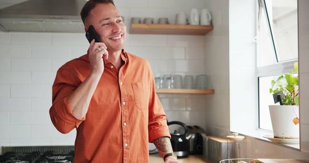 Hombre, cocina y teléfono de llamada o conversación en casa, feliz y relajante en el apartamento. Persona masculina, comunicación y aplicación móvil para una divertida conversación en línea, humor y risa en el teléfono inteligente. - Foto, imagen