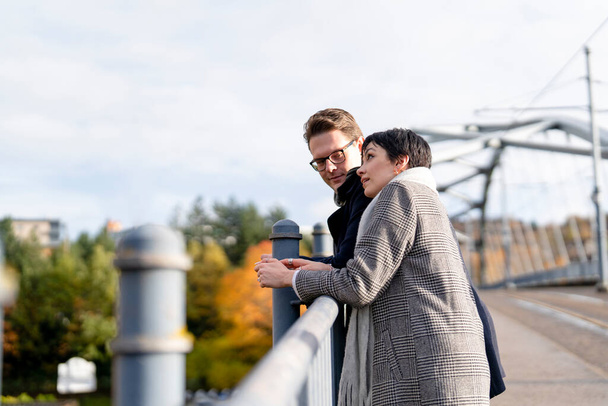 Hombre guapo y mujer hermosa enamorándose, abrazándose, mirando desde un puente mientras caminan alrededor de una ciudad, divirtiéndose, foto de estilo de vida - Foto, Imagen