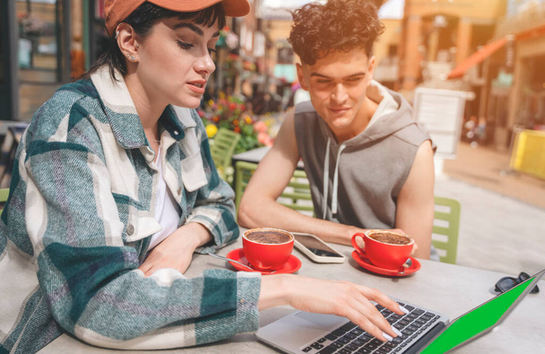 мужчина и женщина сидят в уличном кафе, работают за компьютером и пьют чай и кофе в рамках концепции городского образа жизни - Фото, изображение