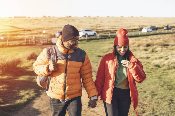 Portrét šťastného zamilovaného páru kráčejícího po venkově při západu slunce. Láska, turistika a aktivní životní styl. tónovaný obrázek - Fotografie, Obrázek