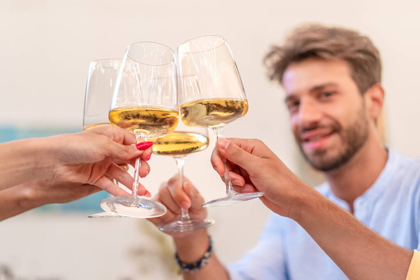 Un groupe d'amis se réunit, levant leurs verres de vin blanc dans un toast pour célébrer une occasion mémorable, incarnant l'esprit de compagnie et de bonne humeur. - Photo, image