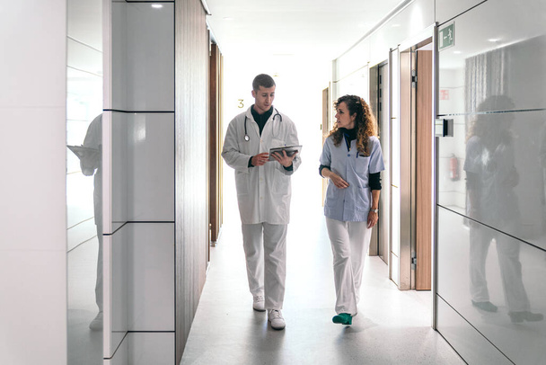 Médico e enfermeiro revisando um gráfico digital em um corredor de hospital brilhante. - Foto, Imagem