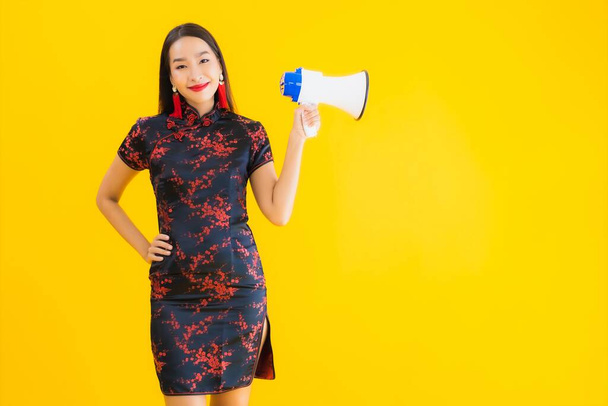 Portrét krásná mladá asijská žena nosit čínské šaty s megafonem na žlutém izolovaném pozadí - Fotografie, Obrázek
