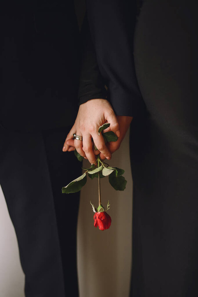 Close up photo of pregnant woman in black dress and her husband holding red rose flower in their hands near pregnant belly. Love concept. Family concept - Photo, Image
