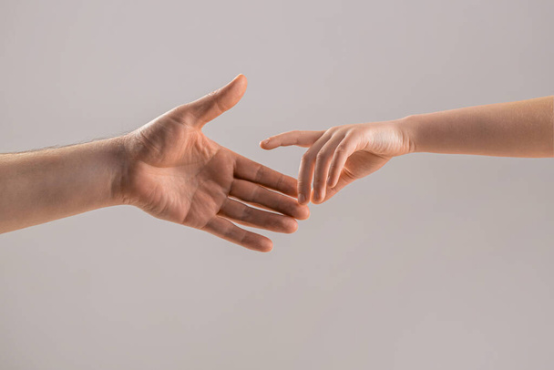 Helping hand concept, support. Help hand outstretched. Man and children hands reach toward each other. Child and father hands isolated on gray. Small childs hand reaches for the hand man. - Photo, Image