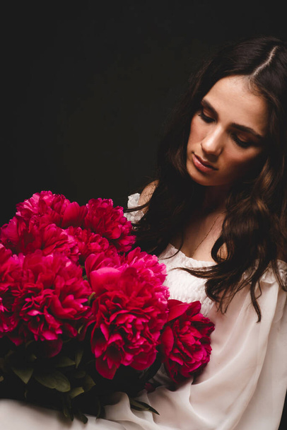 portrait of young, beautiful and sensual woman with a lush bouquet of red peonies in her hands - Photo, Image