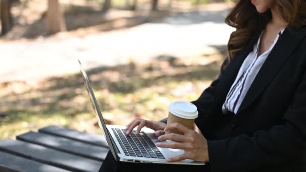 Повільний рух бізнес-леді, що сидить на лавці парку, п'є каву та використовує ноутбук. - Кадри, відео