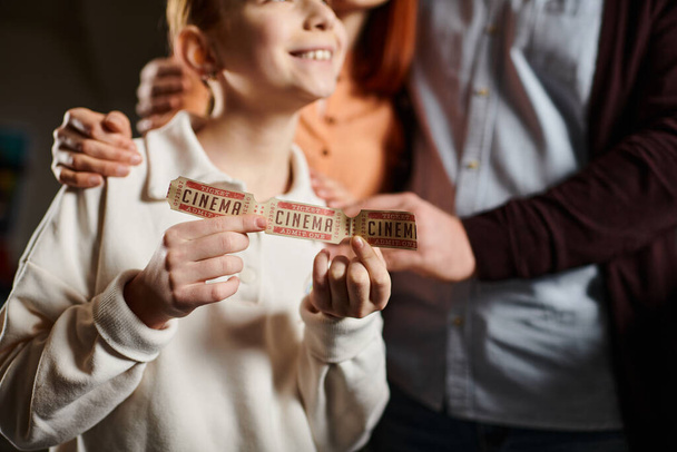Kind hält fröhlich ein buntes Band hoch, das bei einem Kinobesuch die Einheit und Verbundenheit mit der Familie symbolisiert. - Foto, Bild