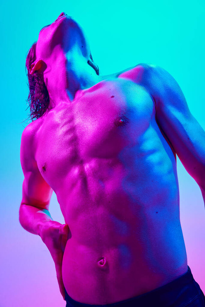 Hombre sin camisa mirando hacia arriba en luz de neón vibrante contra el fondo azul-rosa degradado. Energía de confianza. Concepto de belleza natural personas, fitness, salud y bienestar masculino, masculinidad. - Foto, imagen