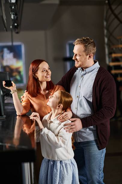 Um homem, uma mulher e uma criança ficam em frente a uma tela de computador, envolvidos em uma atividade compartilhada. - Foto, Imagem