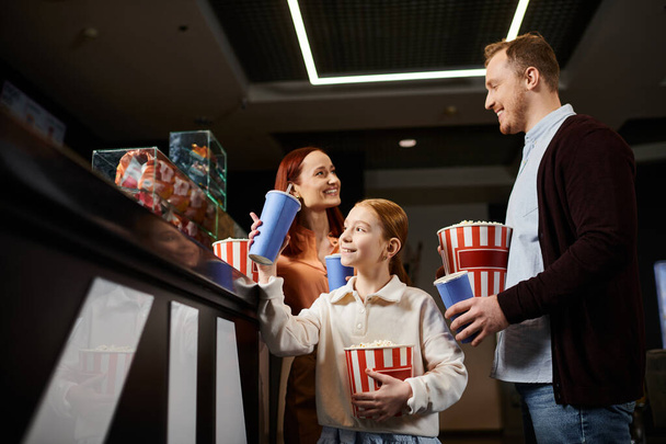 Une famille heureuse debout en cercle, tenant des tasses et bavardant joyeusement dans un décor de cinéma. - Photo, image