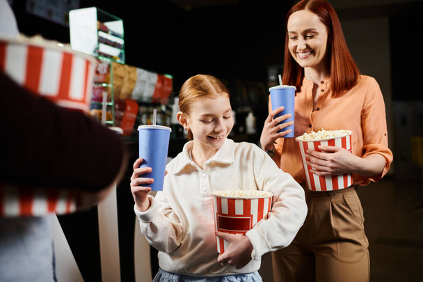 Nainen ja tyttö onnellisesti tilalla kuppeja popcornia viettäessään perheen aikaa elokuvissa. - Valokuva, kuva