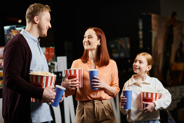 Bir adam ve hir ailesi bir arada, ellerinde patlamış mısır bardaklarıyla sinemada neşe dolu bir anı paylaşıyorlar.. - Fotoğraf, Görsel