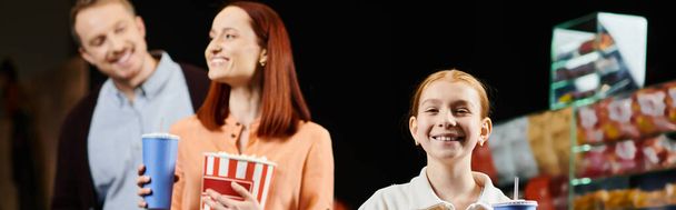 Веселая семья, наслаждающаяся общением в кинотеатре, стоящая бок о бок с сияющими улыбками. - Фото, изображение