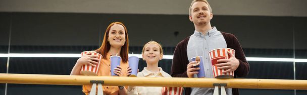 Счастливая семья, стоящая вместе, держащая чашки, наслаждаясь вечером кино в кино. - Фото, изображение
