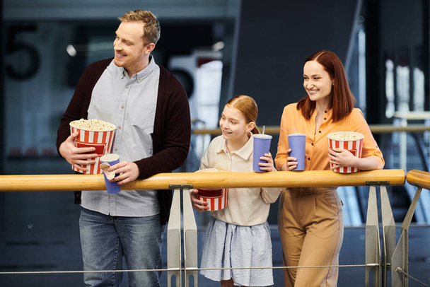 Egy férfi, egy nő és két gyerek boldogan tart popcornt, miközben minőségi időt töltenek együtt egy moziban.. - Fotó, kép