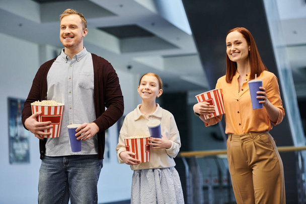 Щаслива сім'я, що складається з чоловіка, жінки та дитини, радісно тримає попкорн, проводячи якісний час разом у кінотеатрі. - Фото, зображення