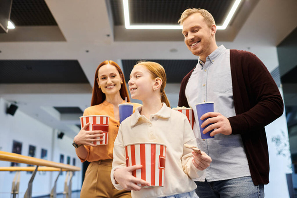 Eine glückliche Familie steht Seite an Seite, jeder hält eine Tasse in der Hand und verbringt Zeit miteinander in einem Kino.. - Foto, Bild