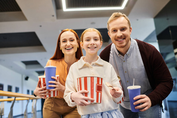 семья улыбается, держа чашки попкорна, сближаясь и наслаждаясь весело провести время кино вместе в кино. - Фото, изображение
