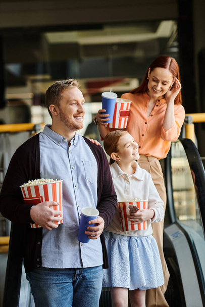 Familie genießt Popcorn, während sie die Rolltreppe hinuntergeht, im Kino, als glückliche Familie. - Foto, Bild