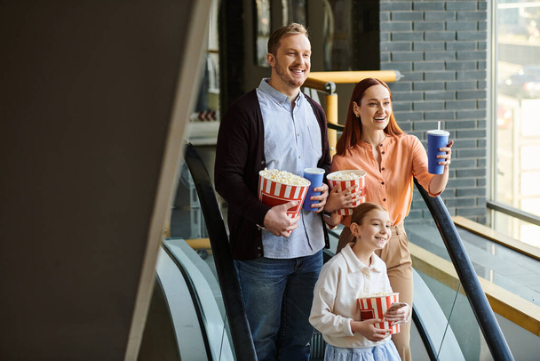 családi állni egy mozgólépcsőn, kezében egy csésze popcorn, élvezi a kirándulást a moziban. - Fotó, kép