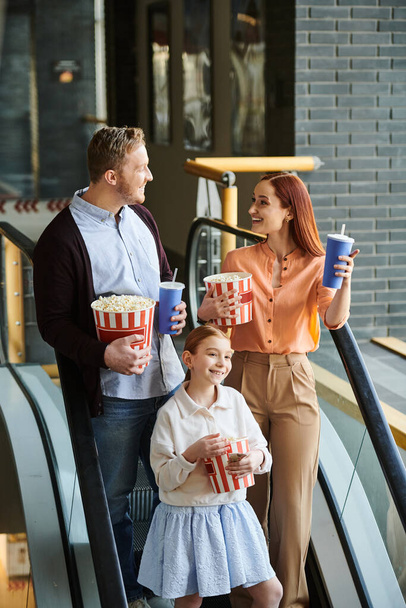 Egy vidám háromtagú család boldogan áll egy emelkedő mozgólépcsőn a moziban, élvezve az együtt töltött időt.. - Fotó, kép