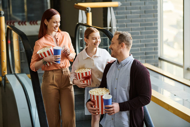 Μια ευτυχισμένη οικογένεια στέκεται συγκεντρωμένη, κρατώντας ο καθένας κουβάδες ποπκόρν, απολαμβάνοντας μια κινηματογραφική έξοδο στο σινεμά.. - Φωτογραφία, εικόνα
