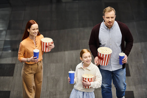 Eine Familie spaziert fröhlich eine Straße entlang und hält nach einem lustigen Kinobesuch Eimer mit Popcorn in der Hand - Foto, Bild