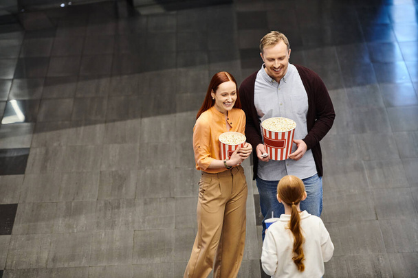 Μια ευτυχισμένη οικογένεια στο σινεμά, κρατώντας ένα κουβά ποπκόρν και απολαμβάνοντας μια ταινία μαζί. - Φωτογραφία, εικόνα