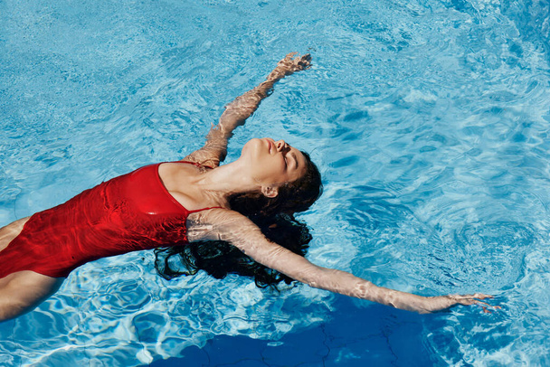 Счастливая женщина плавает в бассейне в красном купальнике с рыжими длинными волосами, защита кожи солнцезащитным кремом, концепция отдыха в отпуске. Высокое качество фото - Фото, изображение