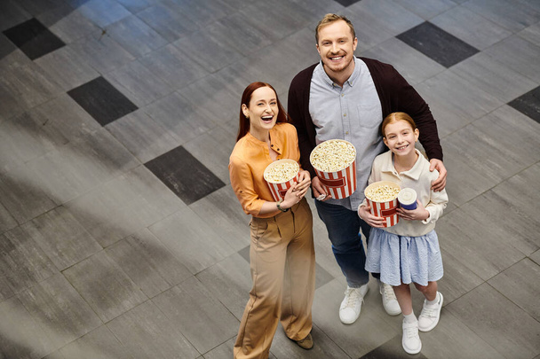 Un homme et sa famille tiennent joyeusement des boîtes de pop-corn au cinéma, profitant d'une soirée cinéma en famille ensemble. - Photo, image