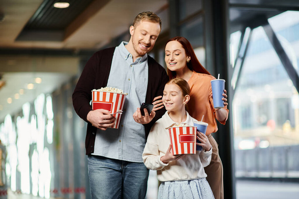 Radosna rodzina w kinie, trzymająca woreczki popcornu razem. - Zdjęcie, obraz
