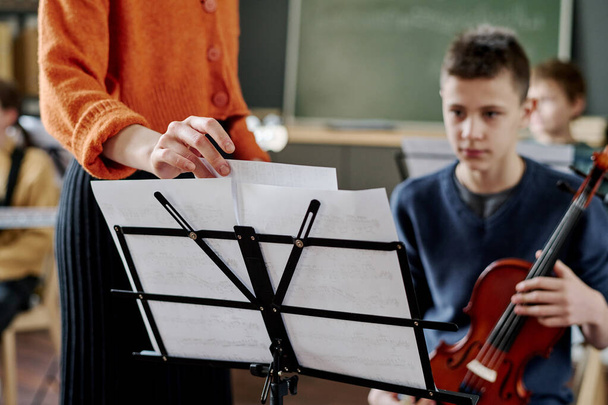 Selective focus shot of unrecognizable female teacher changing sheet music on music stand for boy with violin - Photo, Image