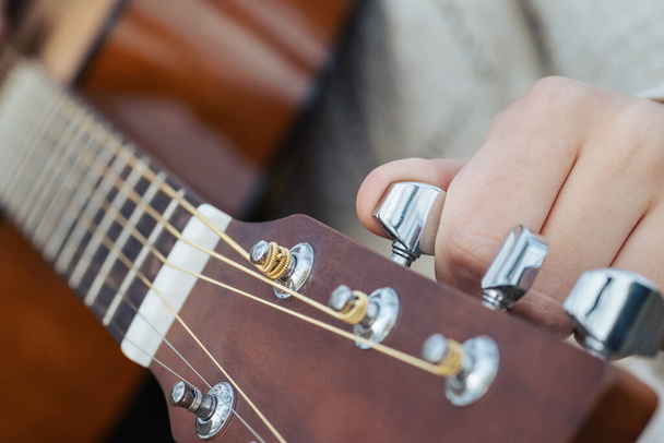 Αλλαγή χορδών κιθάρας από κοντά, ρύθμιση νέων χορδών μιας ακουστικής κιθάρας. Γυναίκα μουσικός κουρδίζοντας κιθάρα, κοντινό πλάνο - Φωτογραφία, εικόνα