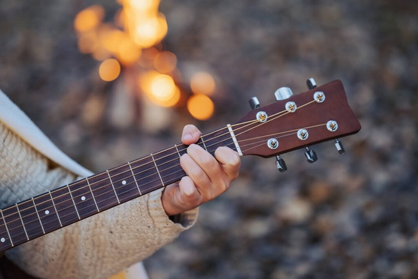 Primer plano en la mano izquierda de una chica guitarrista tocando la guitarra al aire libre cerca de la hoguera. Guitarrista cantando, tocando por la noche en el parque de otoño - Foto, Imagen