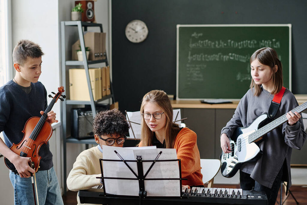 Medium long shot of young music teacher explaining her students how to play part of song during lesson at school - Фото, зображення