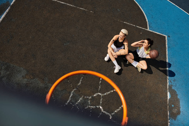 Two young women enjoy a game of basketball on a sunny outdoor court. - Photo, Image