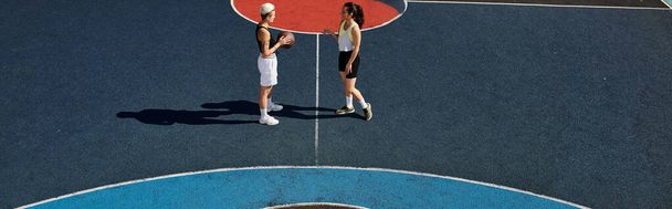 Δύο αθλήτριες στέκονται με αυτοπεποίθηση σε ένα γήπεδο τένις, έτοιμες να διαγωνιστούν κάτω από τον καλοκαιρινό ήλιο.. - Φωτογραφία, εικόνα