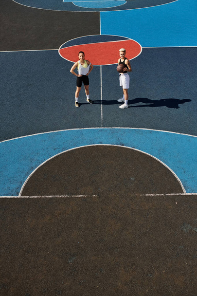 Twee atletische jonge vrouwen die vol vertrouwen op een basketbalveld staan, klaar om de wedstrijd aan te gaan. - Foto, afbeelding
