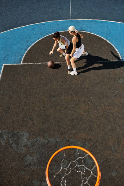 Due giovani donne in abbigliamento sportivo stanno giocando appassionatamente a basket su un soleggiato campo all'aperto. - Foto, immagini