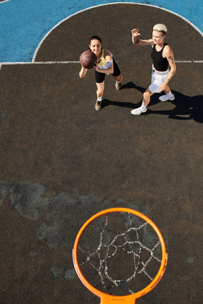 Uma jovem mulher joga basquete em uma quadra, driblando e atirando aros sob o céu ensolarado. - Foto, Imagem