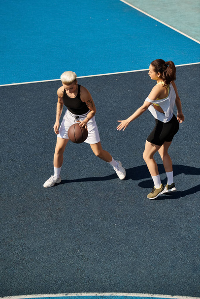 Αθλητικές νεαρές γυναίκες που παίζουν μπάσκετ στο ύπαιθρο μια ηλιόλουστη μέρα, επιδεικνύοντας τις ικανότητές τους και την ομαδική εργασία. - Φωτογραφία, εικόνα