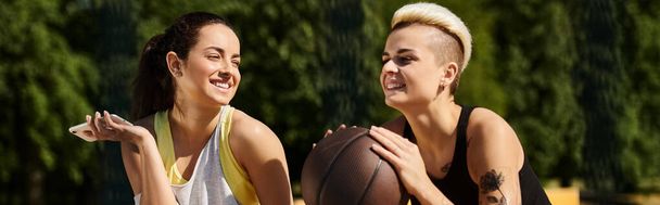 Dwie młode kobiety, przyjaciele i sportowcy, stoją na świeżym powietrzu trzymając koszykówkę, pokazując swoją miłość do sportu. - Zdjęcie, obraz