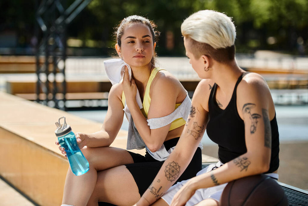 Две молодые спортсменки, друзья, сидят вместе на открытом воздухе после игры в баскетбол летом. - Фото, изображение