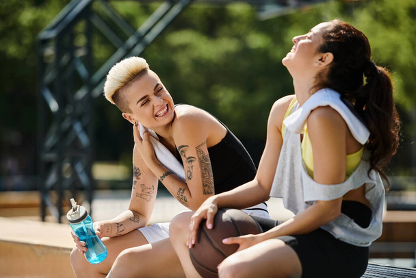 Deux jeunes femmes assises ensemble après avoir joué au basket à l'extérieur, profitant d'un moment d'amitié et de camaraderie. - Photo, image